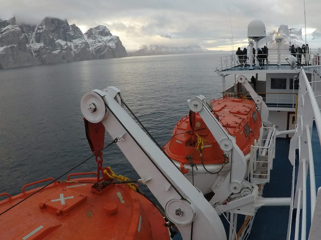 ship sailing through the Northwest Passage on a cloudy day. Seas are calm, cliffs with snow on the side.