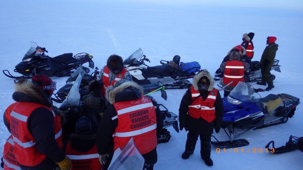 People from the Canadian Ranger patrol standing by snow scooters in the snow