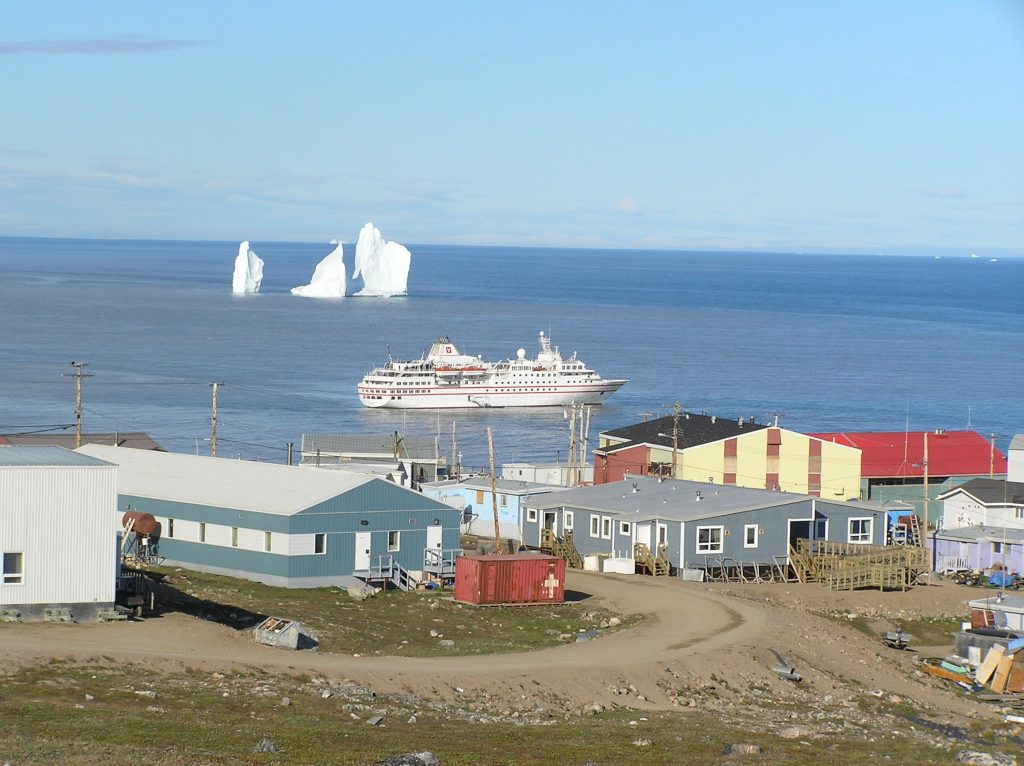 Buildings in the front, with a cruise ship sailing past and icebergs in the distance.