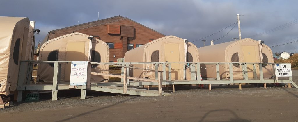 Tents in foreground, with wooden building at the back. Signs to show the different health clinics.